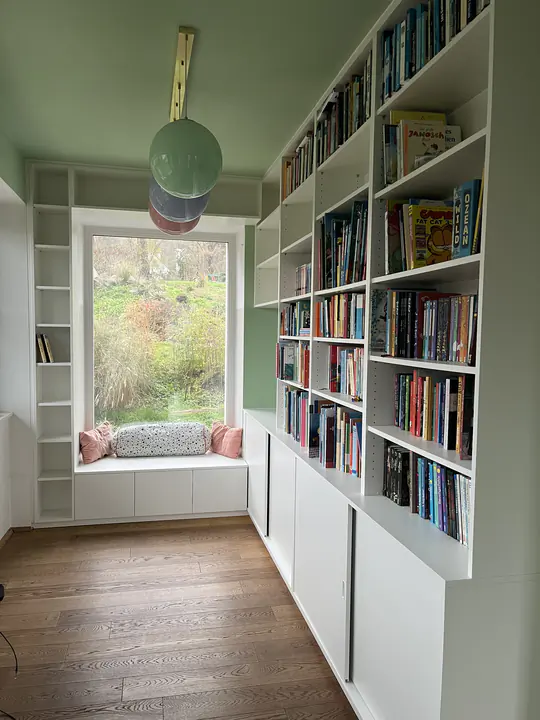 Gesamtblick in dasselbe Bibliothekszimmer, die Regale laufen über Eck auf zwei Wände