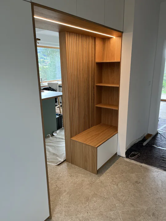 Garderobe aus Eiche mit Lamellenwand, offenen Fächern und Lichtleiste neben einem Durchgang