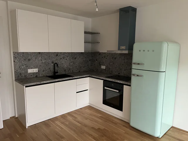 Weiße Küche über Eck mit Steinrückwand, Dunstabzug und mintgrünem freistehendem Kühlschrank