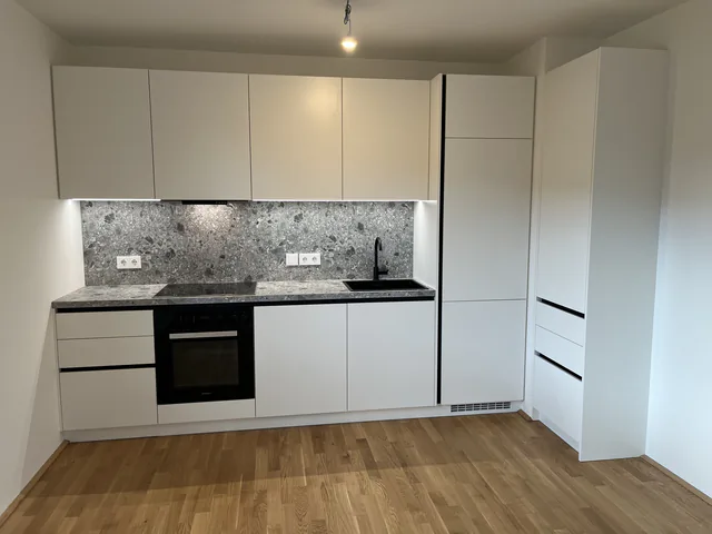 Weiße grifflose Küchenzeile mit Steinrückwand, eingebautem Backofen und dunkler Armatur