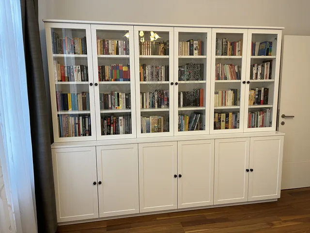 Weiße Bücherwand mit geschlossenen Glastüren über einem geschlossenen Sockelschrank