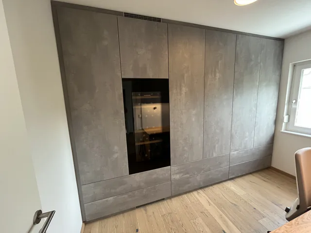 Raumhoher Wandverbau in Betonoptik, von Wand zu Wand gebaut, mit integriertem Glasschrank