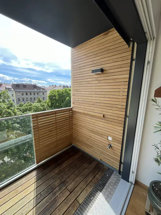 Balkon mit Holzboden und seitlicher Lamellenverkleidung, dahinter der Blick über die Stadt