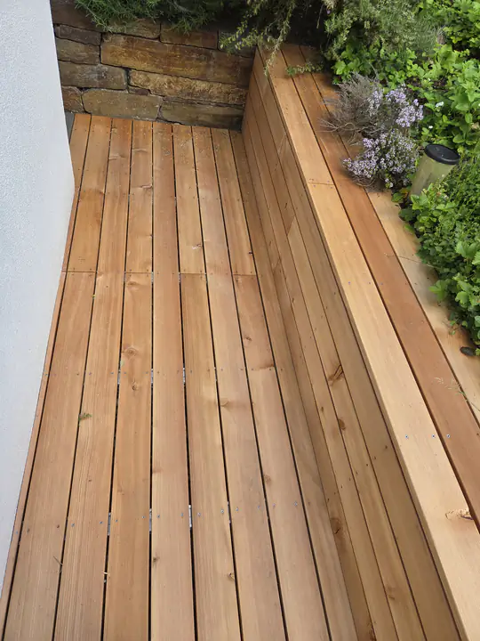 Terrassendielen mit einer umlaufenden Holzsitzbank entlang einer Natursteinmauer