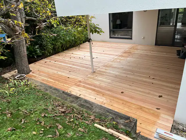 Große neue Holzterrasse aus hellen Dielen vor einem Wohnhaus im Garten
