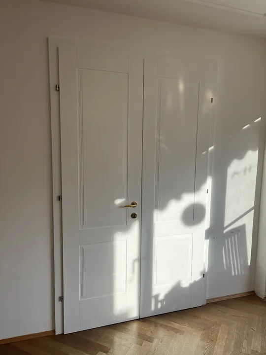 Weiß lackierte Kassetten-Doppeltür in einem Altbau, Sonnenlicht fällt schräg auf das Türblatt