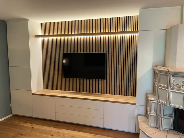 TV-Wand mit beleuchteter Akustik-Lamellenfläche über einem Sideboard